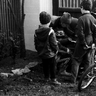 Three teens leaning against fence near parked bicycle.