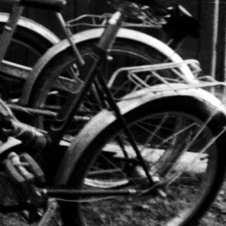 Three teens leaning against fence near parked bicycle.