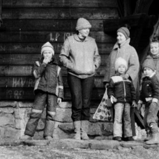 Family posing outdoors near rustic wooden cabin.