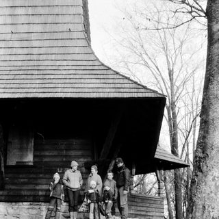 Family posing outdoors near rustic wooden cabin.