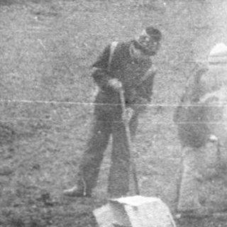 Two people extinguishing a small outdoor fire.