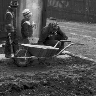 Two men pushing wheelbarrow near concrete structure.