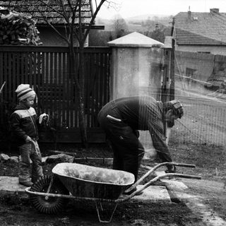 Three people mixing concrete with wheelbarrow.