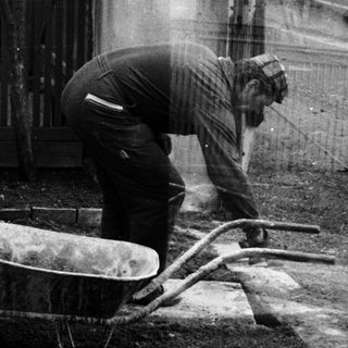 Three people mixing concrete with wheelbarrow.