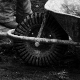 Three people mixing concrete with wheelbarrow.