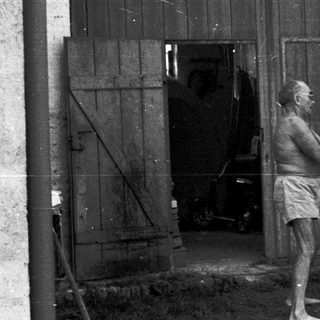 Man sawing wood outside rustic wooden building.