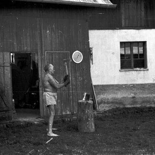 Man sawing wood outside rustic wooden building.