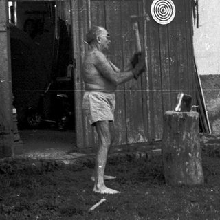 Man sawing wood outside rustic wooden building.