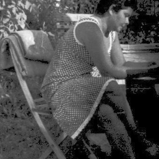 Person reading outdoors on chair near garden.