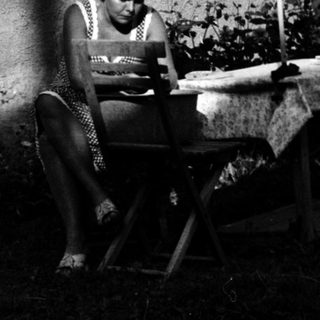 Person reading outdoors on folding chair near house.