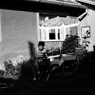 Person reading outdoors on folding chair near house.