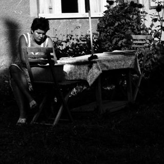 Person reading outdoors on folding chair near house.