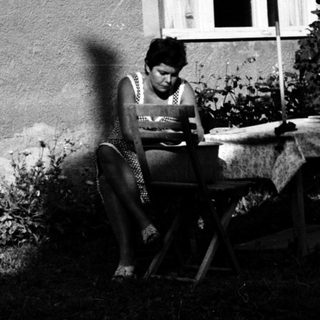 Person reading outdoors on folding chair near house.