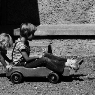 Two children playing with a toy car outdoors.