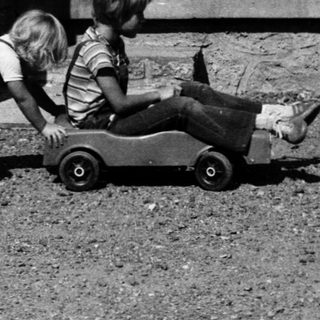 Two children playing with a toy car outdoors.