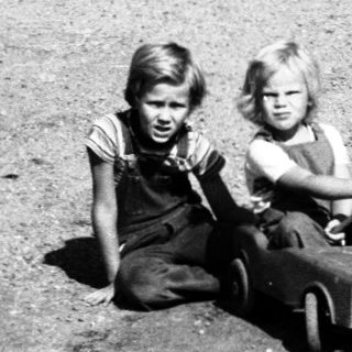 Two children playing with toy cars on gravel road.