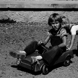 Child pushing another child on a toy wagon.