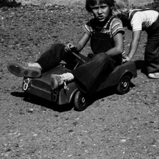 Child pushing another child on a toy wagon.