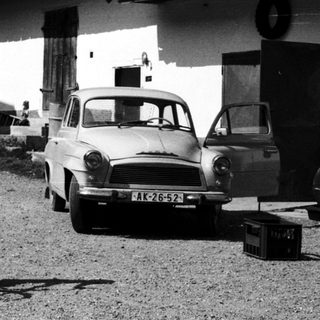 A boy rides a bicycle in a gravel driveway near vintage cars.