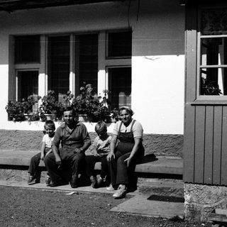 Family posing outside a house in vintage clothing.