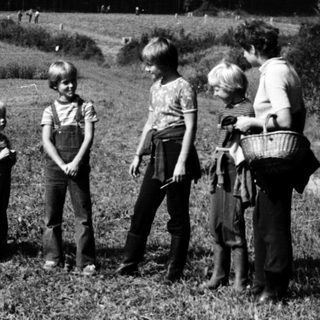 Children and adults in rural field near forested hill.