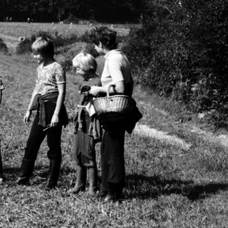 Children and adults in rural field near forested hill.