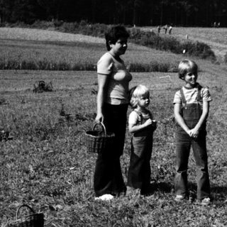 Children and adults in rural field near forested hill.