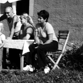 Family sitting outdoors near a house with umbrella.