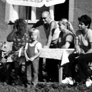 Family sitting outdoors near a house with umbrella.