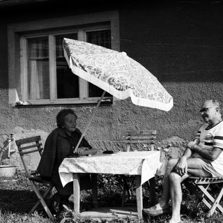 Two people sitting outdoors under umbrella, enjoying conversation.