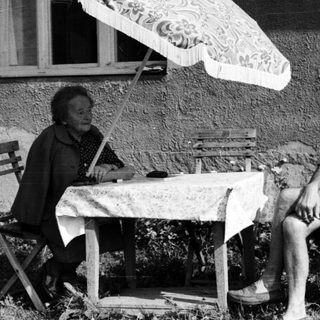 Two people sitting outdoors under umbrella, enjoying conversation.