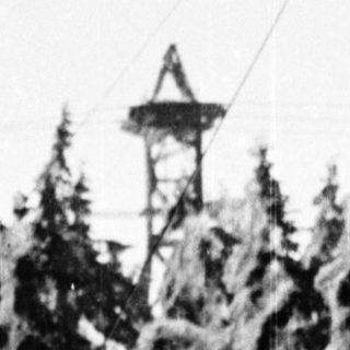 Snow-covered forest with frozen trees and a small tower.
