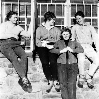Four people posing together outdoors in 1960s-style clothing.