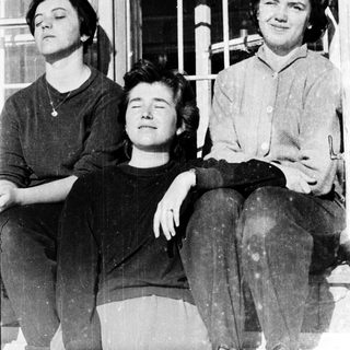 Three women sitting closely together, posing outdoors.