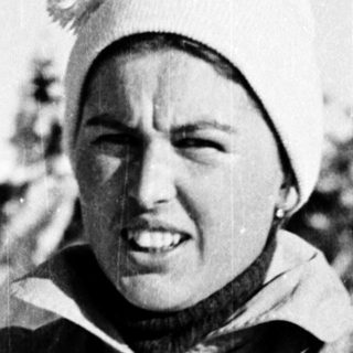 Woman in winter attire, holding ski poles.