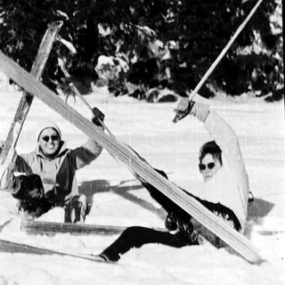 Two people skiing on snow, one lying down.