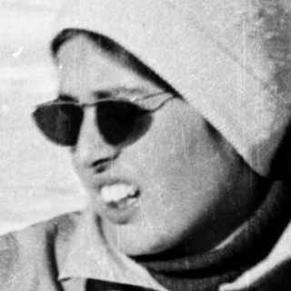 Person skiing in snowy terrain wearing sunglasses and winter gear.