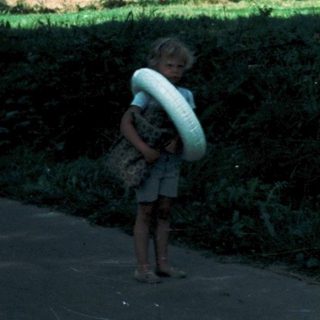 Rural roadside scene with child and dog by fields and hill.