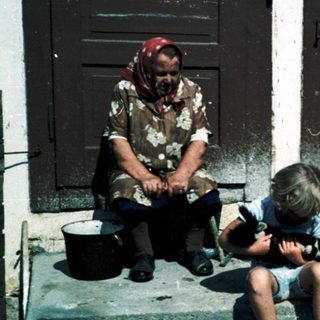 Rural scene: woman with children and dog outside.