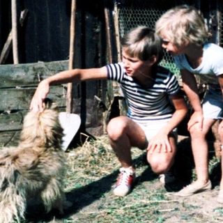 Two children petting a sheep in rural barn area.