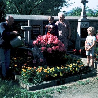 Family tending gravesite with flowers in cemetery.