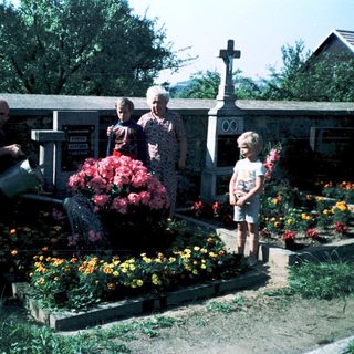 Family tending gravesite with flowers in cemetery.