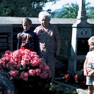 Family tending gravesite with flowers in cemetery.