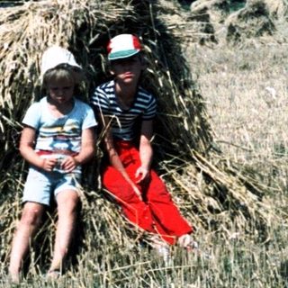 Two people posing behind large haystacks in field.