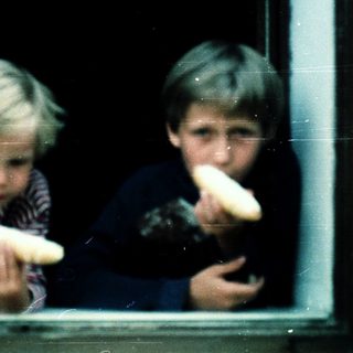 Two children eating bread through a window.