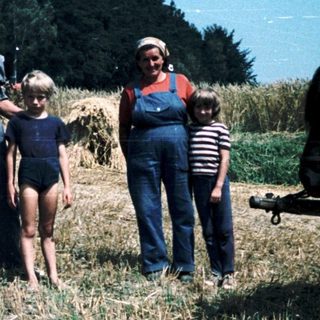 Family posing with horse-drawn hay wagon in rural field.