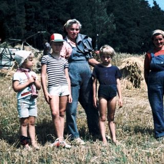 Family posing with horse-drawn hay wagon in rural field.