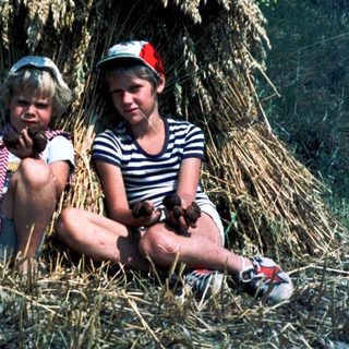 Two children sitting under a haystack.