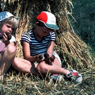 Two children sitting under a haystack.
