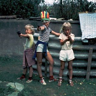 Three children playing with toy guns outdoors.